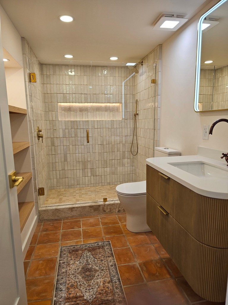 Finished casita bathroom with vertical tile shower, brass hardware, and terracotta floors