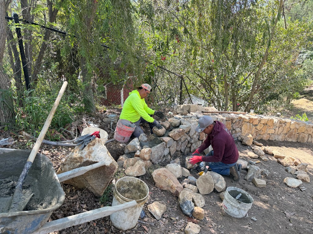 CRG crew laying a stone wall with light mortar on a concrete footing